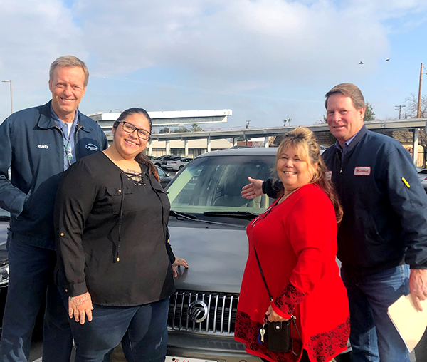 Photo of Marina standing with Nancy (Early Head Start Child Development Specialist) in front of Randy and Michael from Fresno Select Group by the prize van.