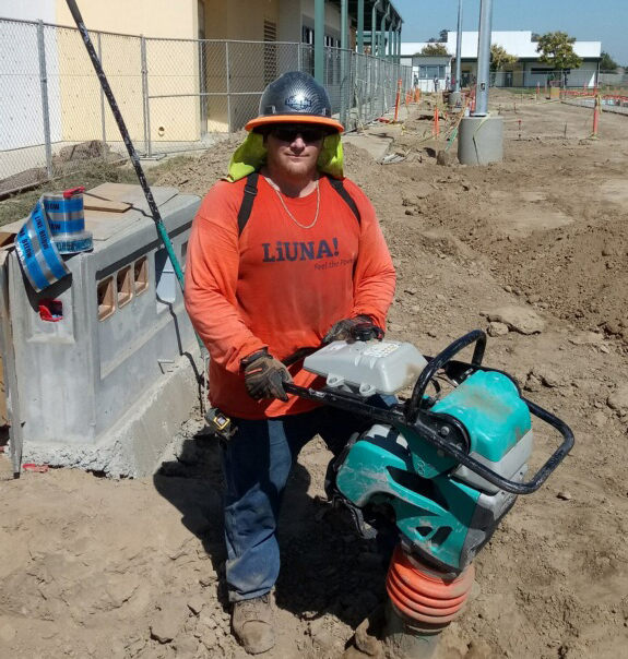 Travis wearing safety gear and holding a jack hammer on a job site